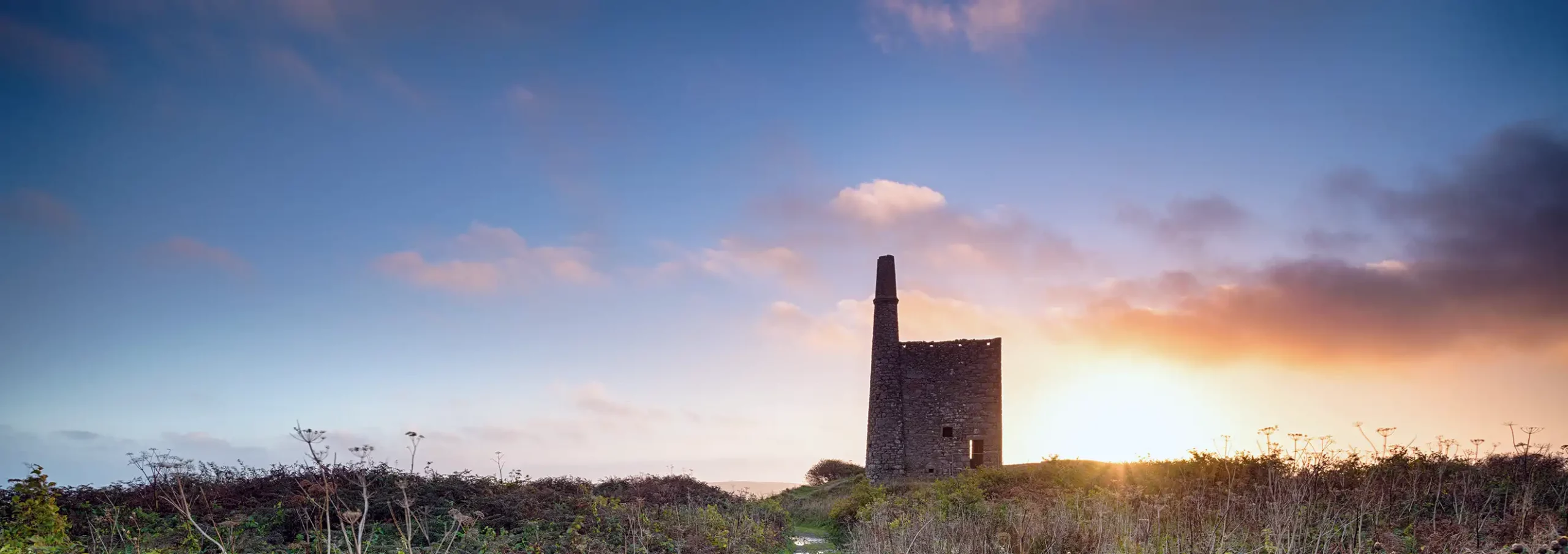 Sunset over Ding Dong Mine, an iconic Cornish engine house near Penzance — surrounded by wild hedgerows and rural landscape.