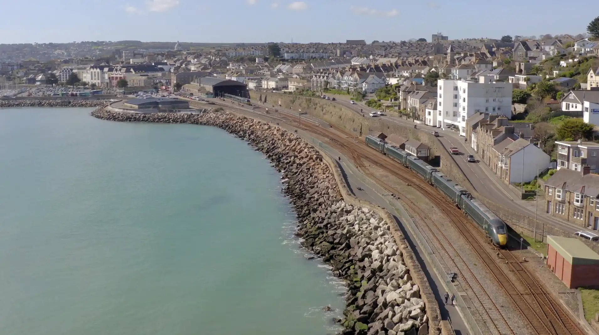 Aerial view of Penzance seafront and railway line, with the town centre and housing rising inland — showcasing Cornwall’s westernmost transport hub.