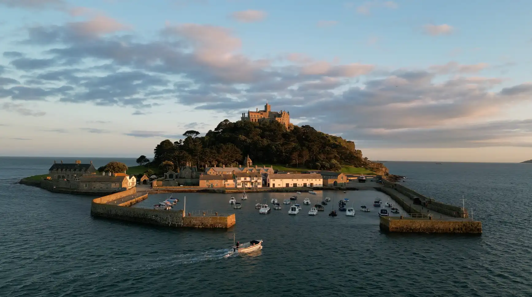 St Michael’s Mount at sunset, with boats moored in the harbour and the castle rising above the island — a well-known tidal landmark off the coast of Marazion, Cornwall.