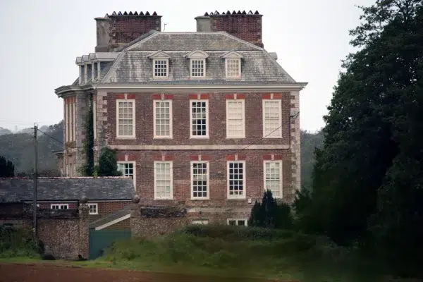 Front view of Puslinch House, a historic Victorian manor in Cornwall, showing its grand brick façade and surrounding grounds.
